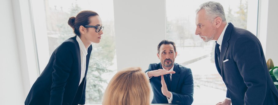 Deux collaborateurs ayant un désaccord, un conflit, debout l'un devant l'autre, face à face avec une expression d'irrespect, la personne au milieu joue le rôle de médiateur et fait un signe d'arrêt avec les mains.